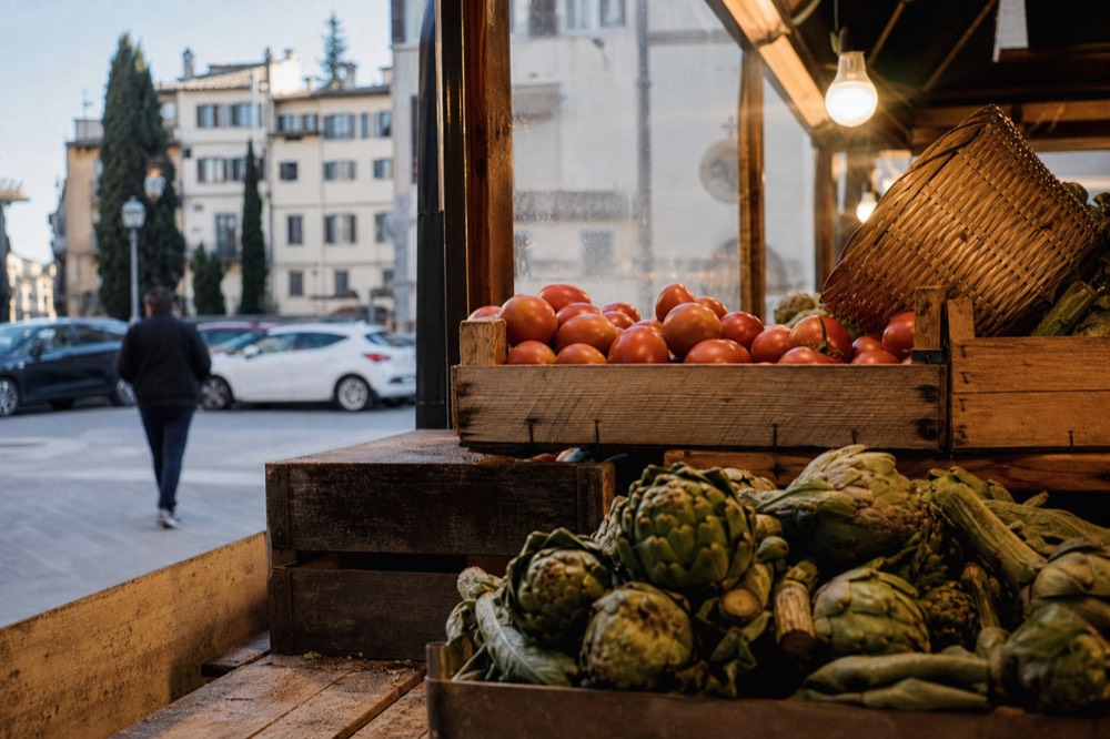 A wooden market stall piled with fresh produce under warm lights