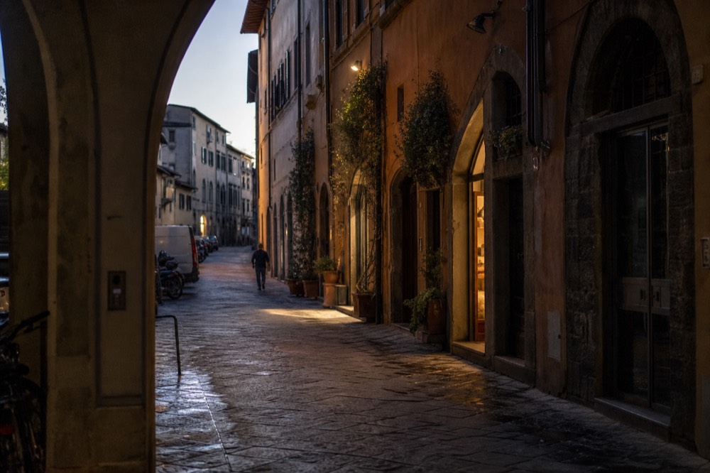 A narrow Florentine street at dusk with lit shopfronts and stone buildings