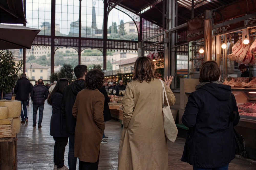 A guide speaking to a small group beside a food stall in a Florence market hall