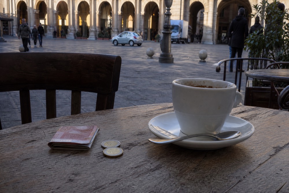 Coins and a small note beside an espresso cup on a wooden cafe table