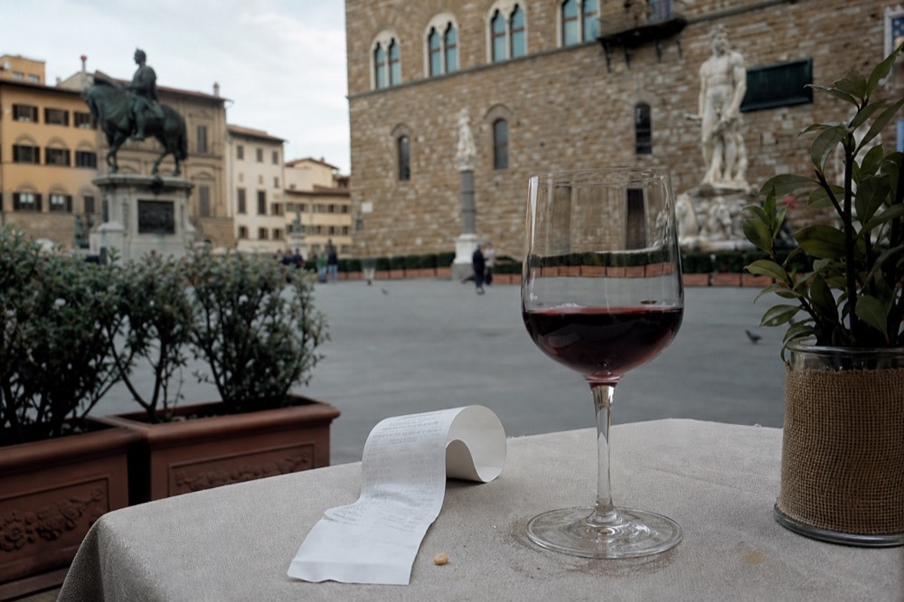 A printed restaurant bill resting beside a glass of red wine on a set table