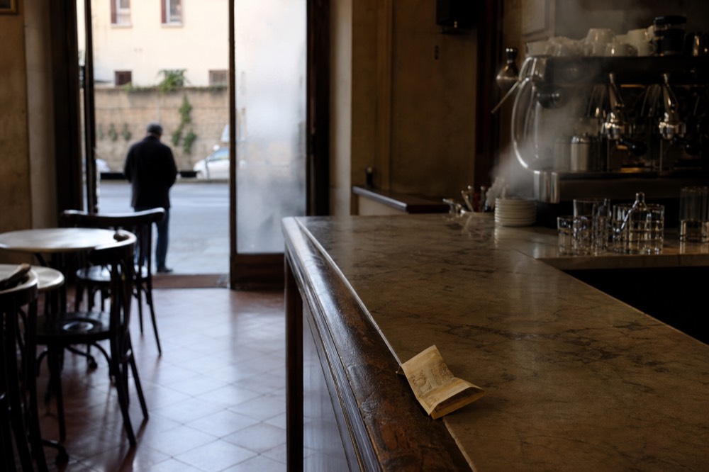 A hand passing a folded banknote across a marble counter in an Italian bar
