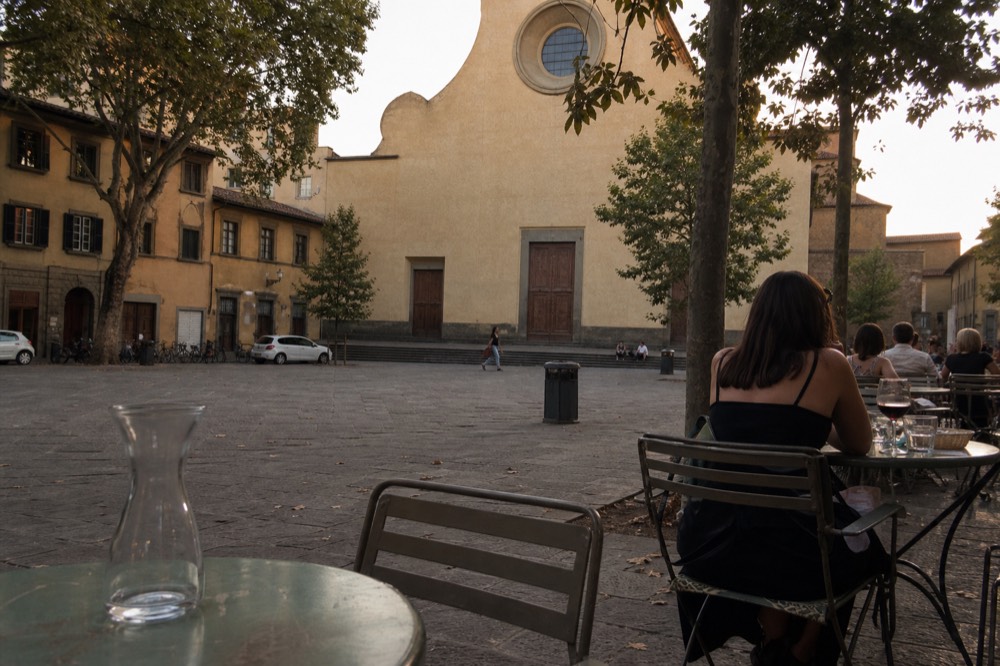 Piazza in the Oltrarno district with a church facade and simple outdoor tables on the pavement