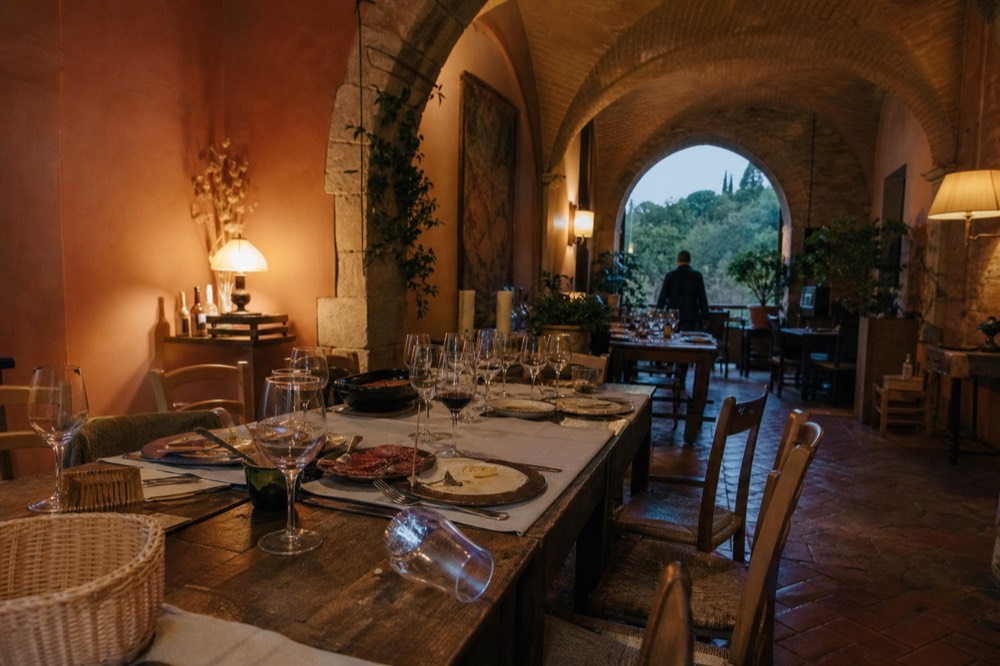 A long wooden table set with wine glasses and Tuscan dishes in a warm dining room