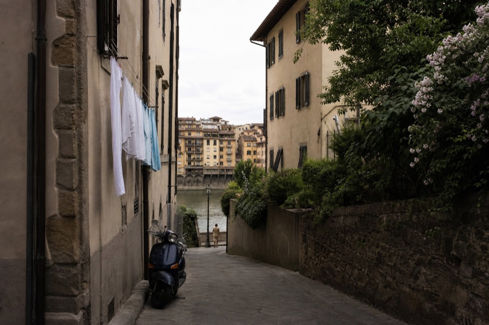 A narrow Florence street with stone buildings leading toward the Arno river