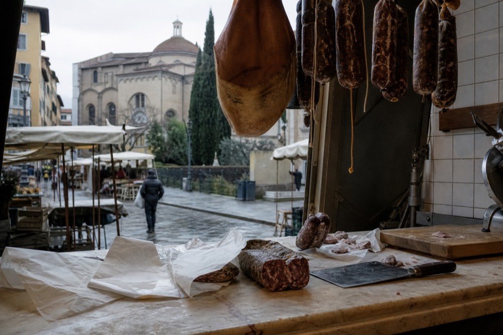 Assorted cured salamis and whole hams hanging in an Italian delicatessen display
