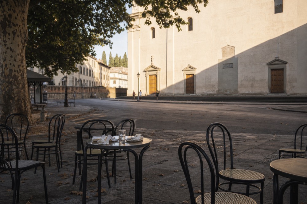 Empty café tables and chairs on a Florence piazza in morning light