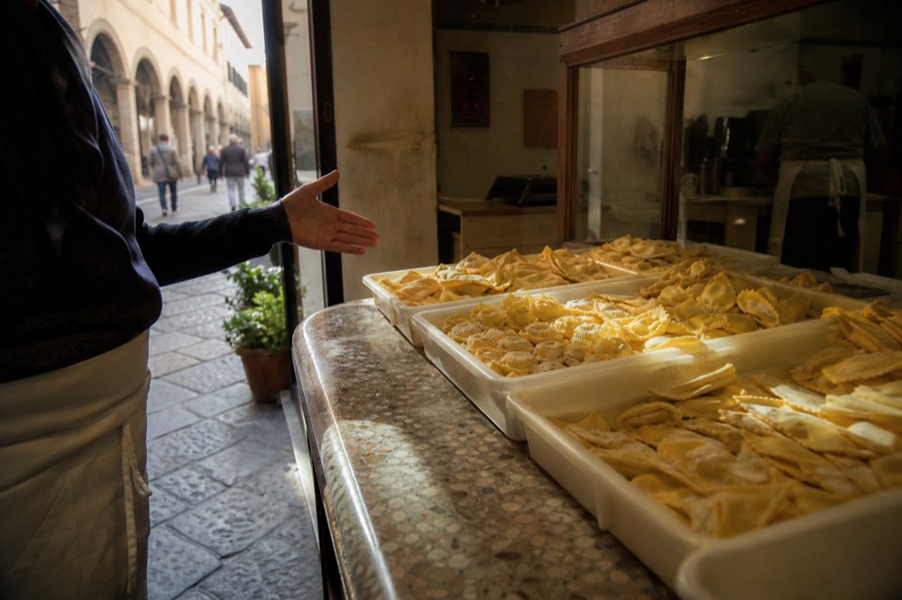 A guide gestures toward a display of fresh pasta in a Florence food shop