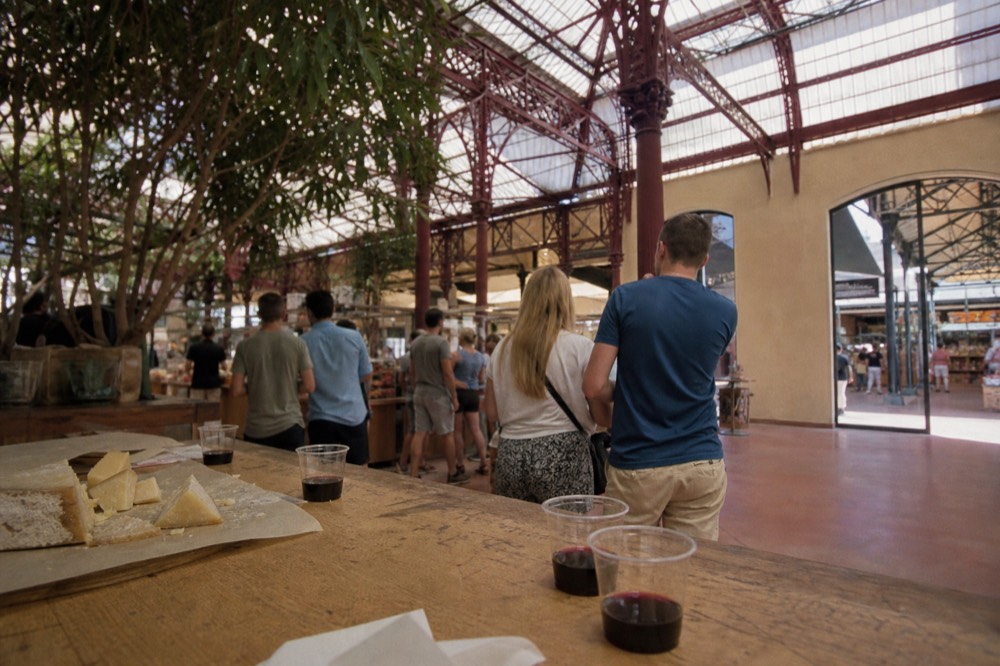 A food tour group gathers around a vendor at the Mercato Centrale, tasting cheese