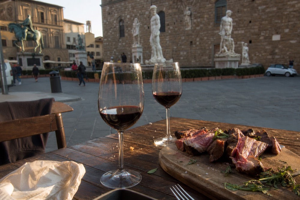 Slices of grilled steak and glasses of red wine arranged on a rustic restaurant table
