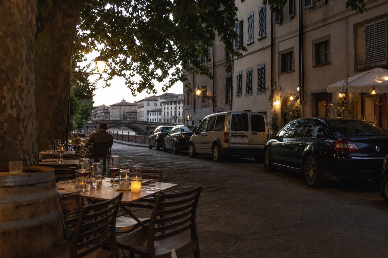 Evening tables with wine glasses and small plates set along a Florence street