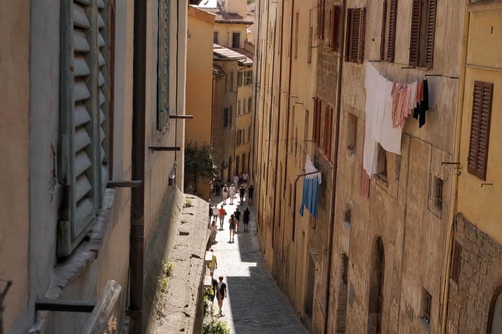 Crowded narrow Florence street with pedestrians between tall stone buildings