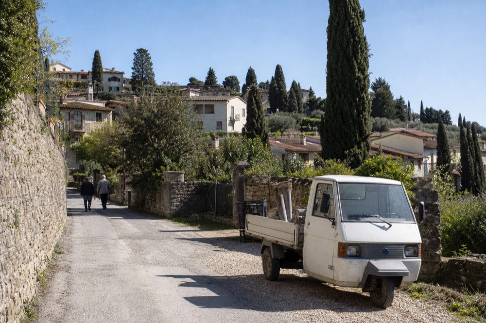 A hilltop Tuscan town with stone buildings and cypress trees under a clear sky