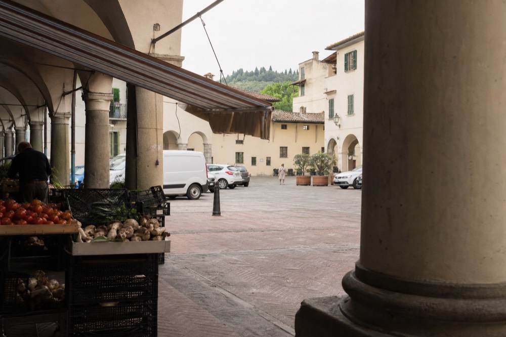 A covered market square with stalls of produce and canvas awnings in a Tuscan town