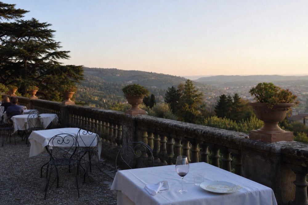 A villa terrace with white tablecloths overlooking wooded hills above a valley