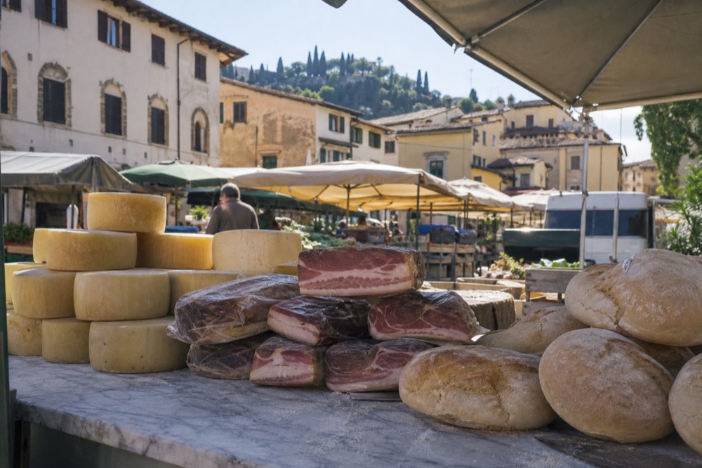 A market counter stacked with Tuscan cheeses, cured hams and rounds of unsalted bread