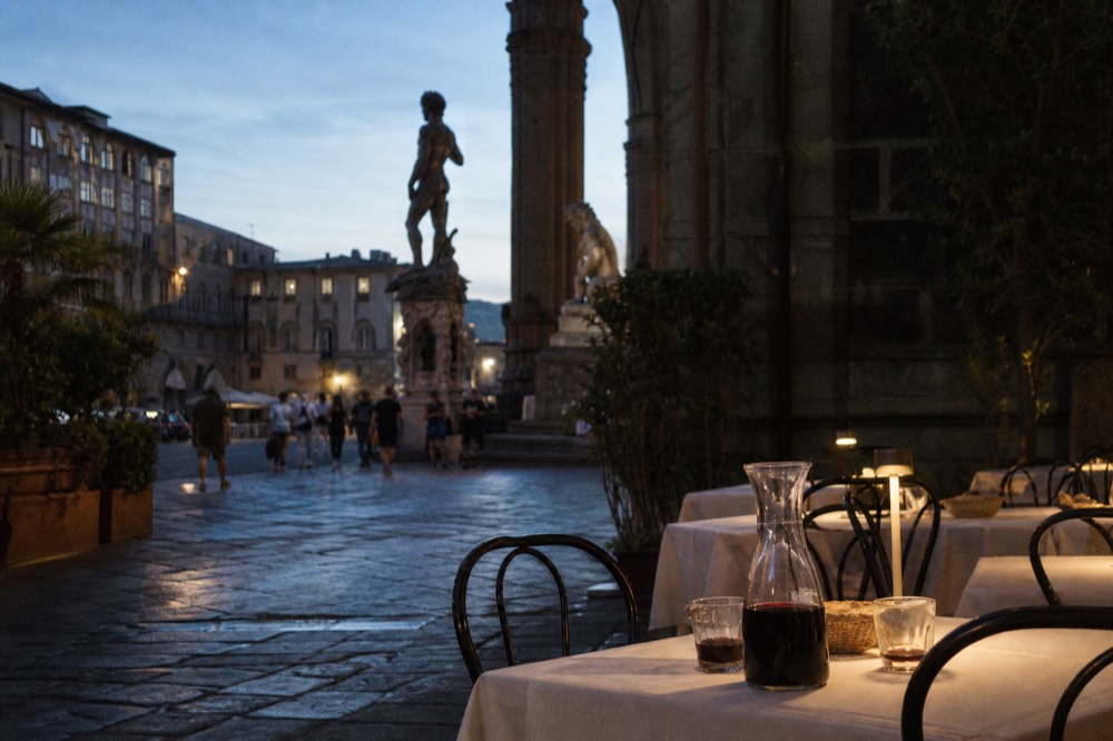 An evening piazza in Florence with restaurant tables and warm light on old buildings