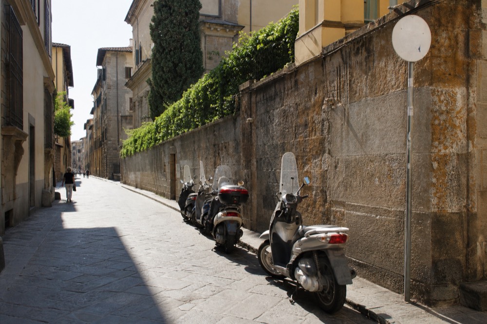 A Florence street with a limited traffic zone sign above parked scooters and old stone walls