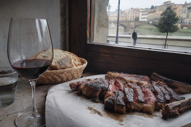 Seated table in a Florence trattoria, Italy, with a sliced Florentine steak, bread and a glass of red wine.