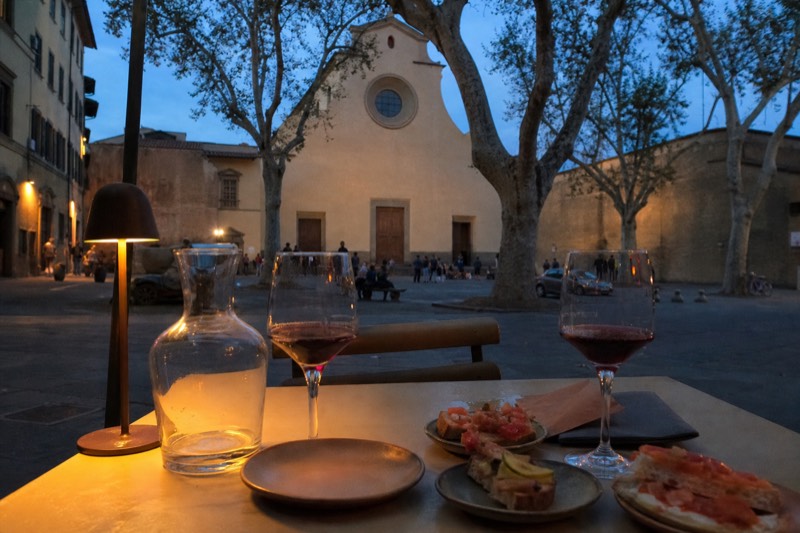 Evening street table in the Oltrarno district of Florence, Italy, with small plates and wine glasses under warm light.