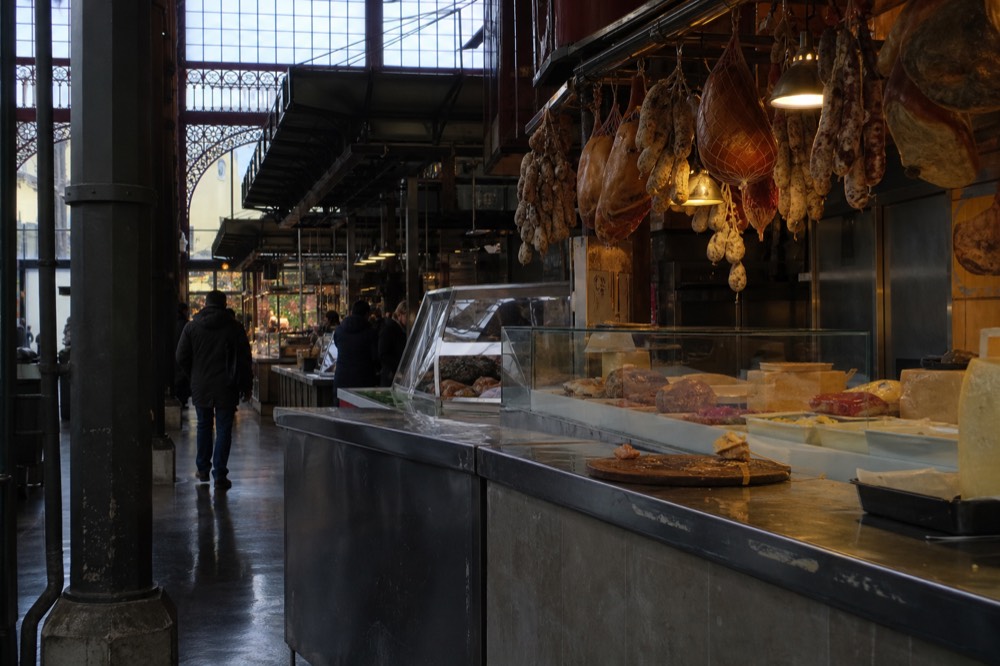 Covered market interior with food stalls and hanging cured meats