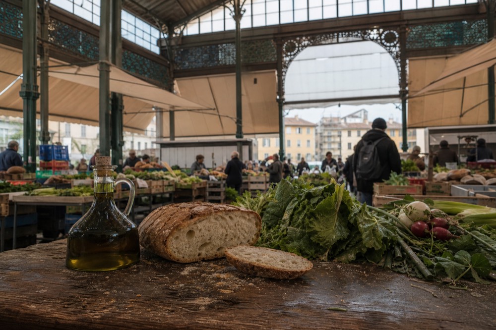Rustic wooden table with olive oil bottle, bread loaf and fresh vegetables