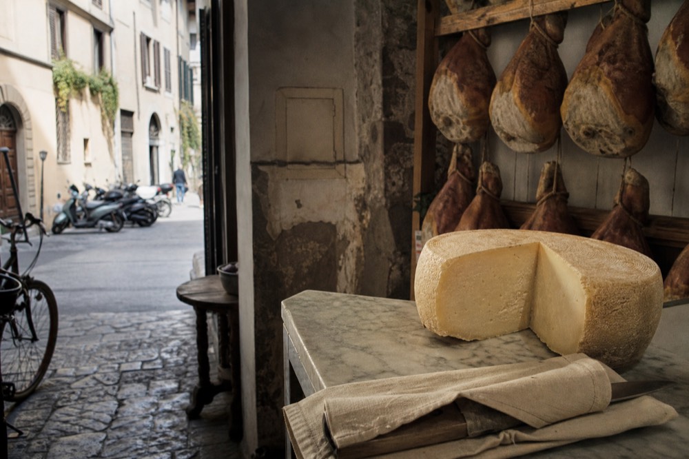 Wheel of aged cheese and whole cured hams in a traditional Italian delicatessen