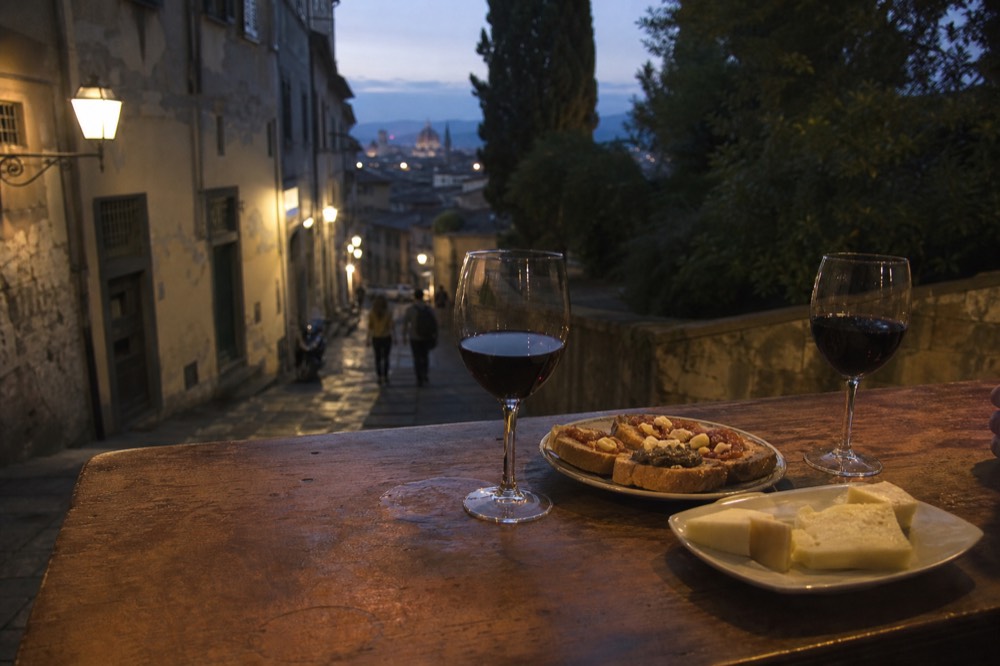 Glasses of red wine and plates of Tuscan appetisers on a wooden counter at night