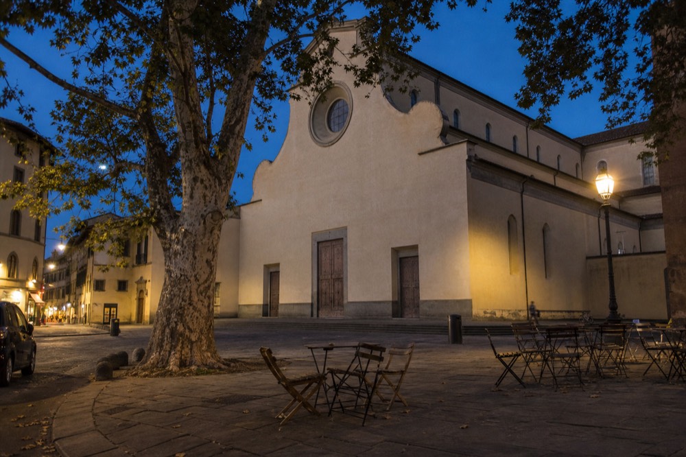 Piazza Santo Spirito at dusk with the basilica facade and empty tables under lamplight