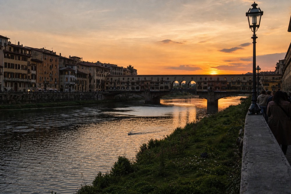 Warm evening light on the Arno river with Ponte Vecchio silhouetted against an orange sky