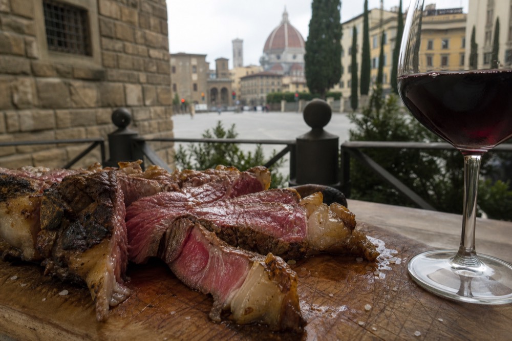 Sliced Florentine steak on a wooden board beside a glass of red wine