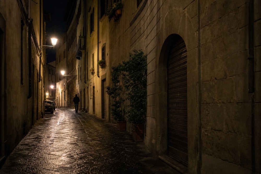 Illuminated Florence street at night with lamps reflecting on stone buildings