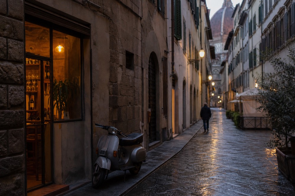 A narrow Florentine street with stone buildings and a small enoteca window at dusk