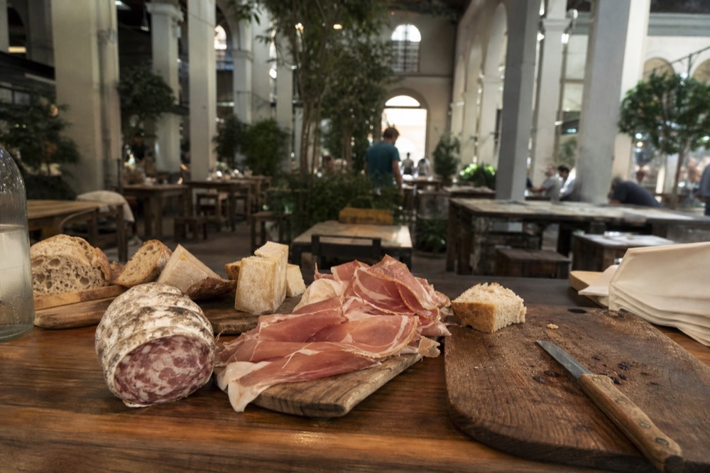 Plates of cured meat, cheese and bread arranged along a wooden bar top