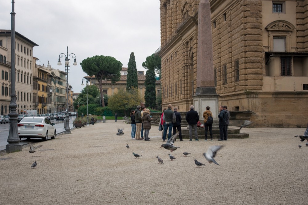 A small group of walkers with a guide standing in a Florence piazza near a stone building