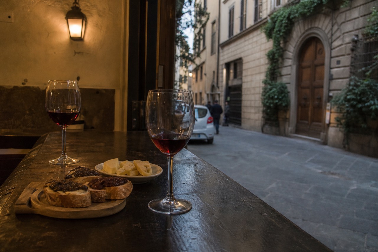 Glasses of red wine and plates of Tuscan appetisers on a wooden counter in a Florentine wine bar