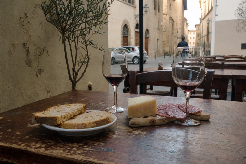 A table set with Tuscan bread, pecorino cheese, salami and glasses of red wine