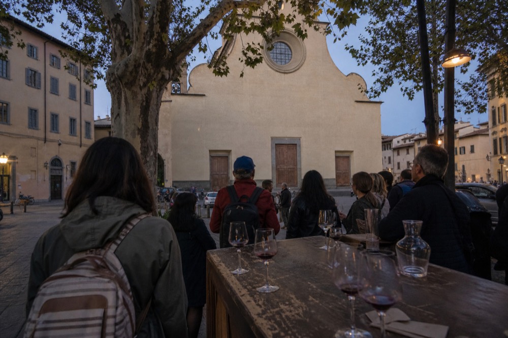 An evening food tour group at a wine counter with glasses of Tuscan red wine at dusk