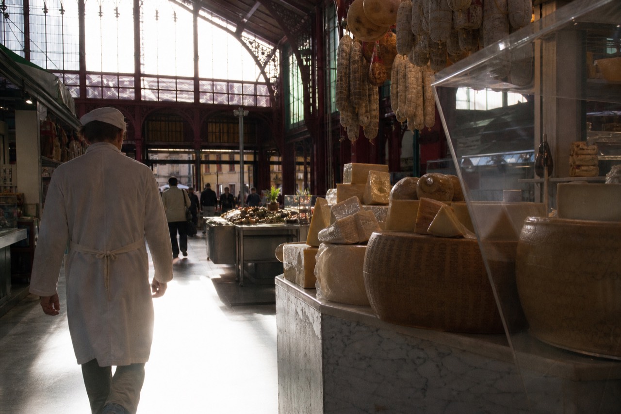 A covered Florence food market hall with stalls of cheese, bread and cured meats under iron and glass architecture