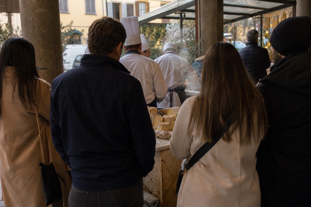 A chef-led tasting group gathered around a cheese and charcuterie stall inside a market