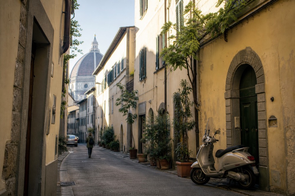 A narrow Florentine street with stone buildings and distant dome