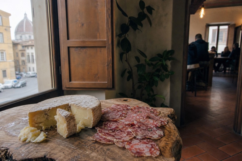 A close-up of a wheel of pecorino cheese and sliced finocchiona salami on a wooden board