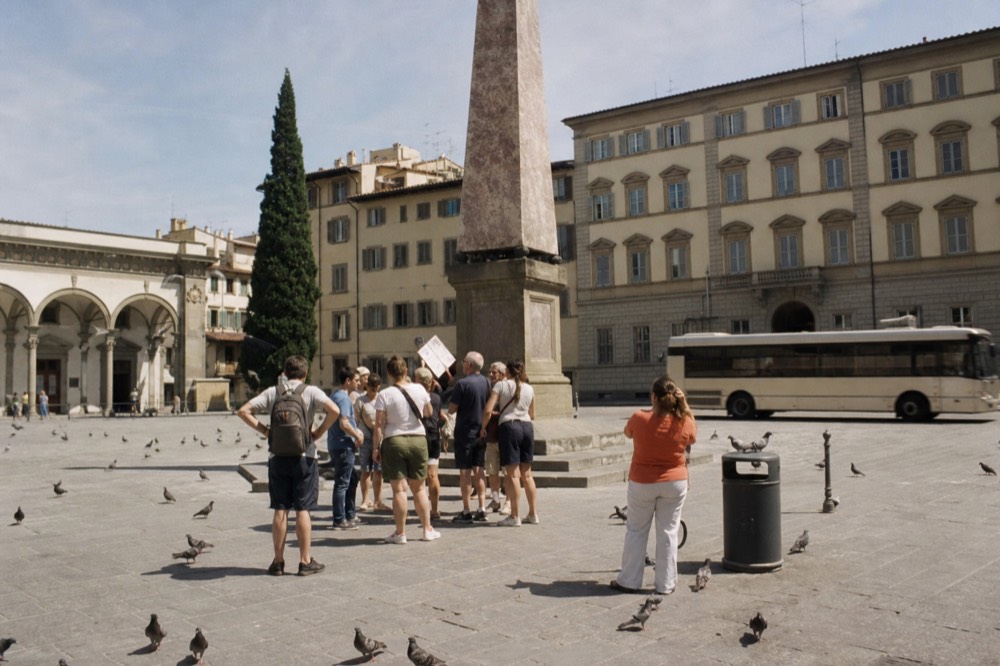Piazza dell'Unita Italiana with the obelisk in the centre, a small group gathering with a guide holding a sign