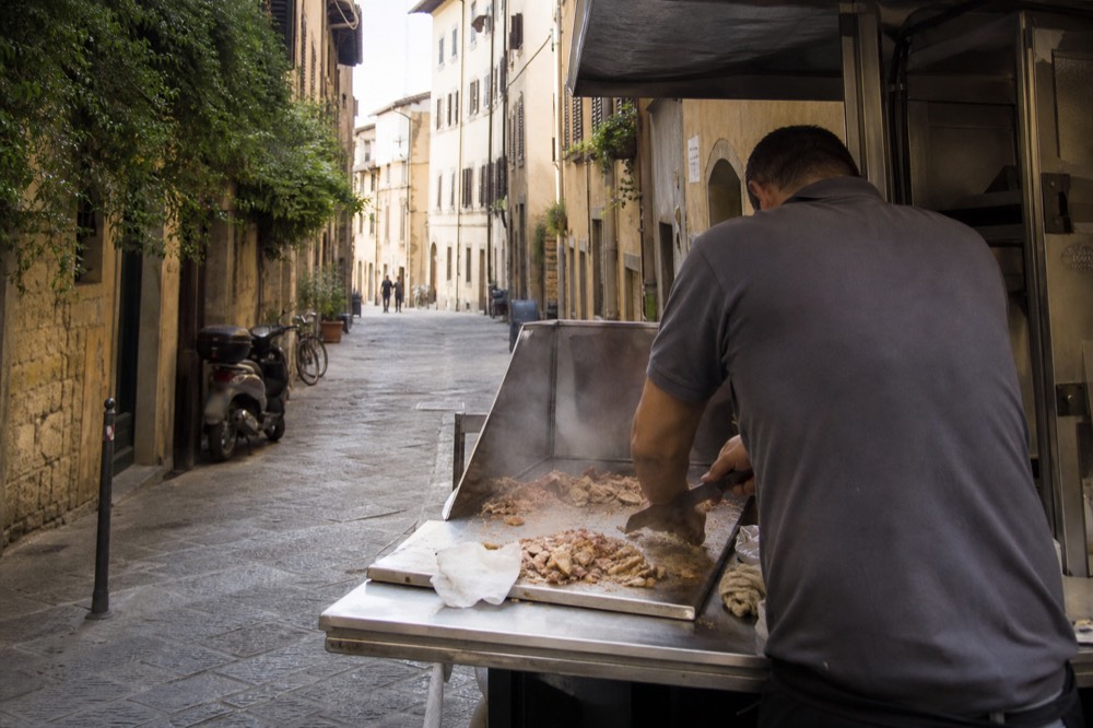A lampredotto stall with a vendor slicing meat into a bread roll