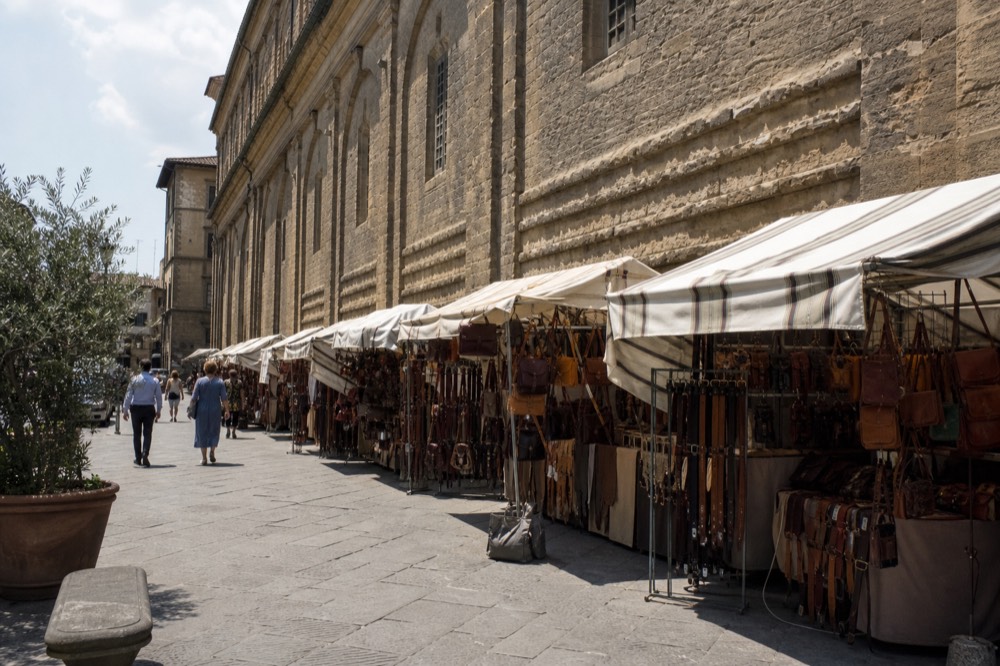 A Florence street with a row of market stalls selling leather goods