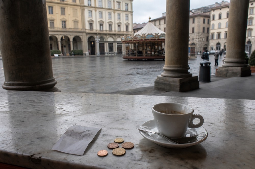A receipt and coins beside an espresso cup on a marble bar counter