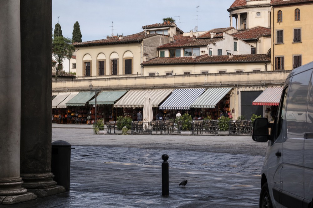 A sunlit Florentine street with market awnings and café tables in the morning