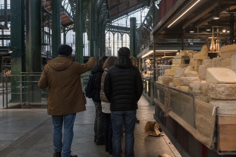 A guide leading a small group through a Florentine market, pointing at a cheese stall