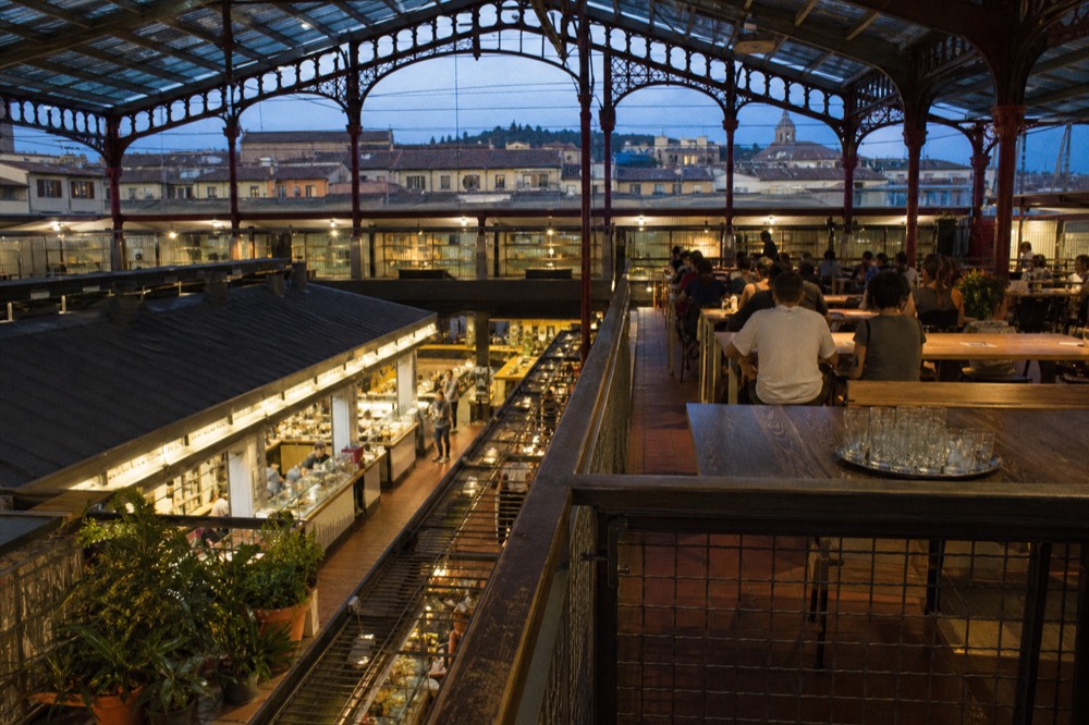 Food hall seating area beneath an iron and glass roof with food stalls along the aisles