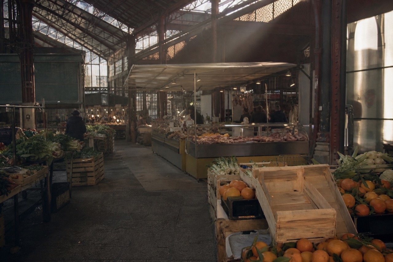 Interior of a historic cast-iron market hall with food stalls under a glass roof